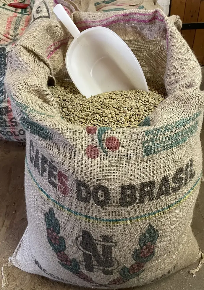 Feinkost Kaisen - Jutesack gefüllt mit Arabica Rohbohnen. Dekoratifv ist eine weiße Lebensmittel Schaufel in den Kaffee gesteckt