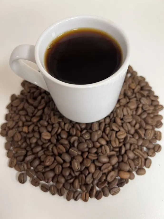 Feinkost Kaisen - Frisch gebrühte Tasse Kaffee auf einem Bett aus gerösteten Kaffeebohnen